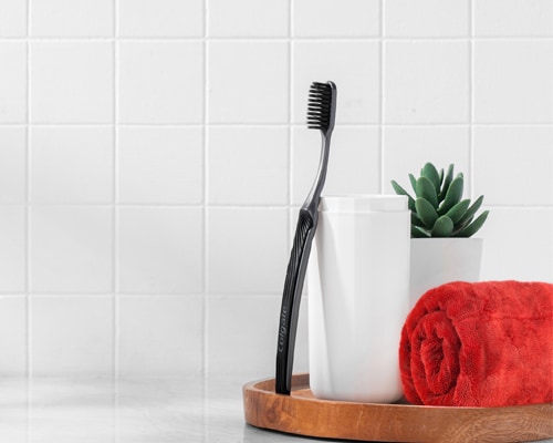 Berus Gigi Colgate SlimSoft Charcoal bersandar pada cawan
