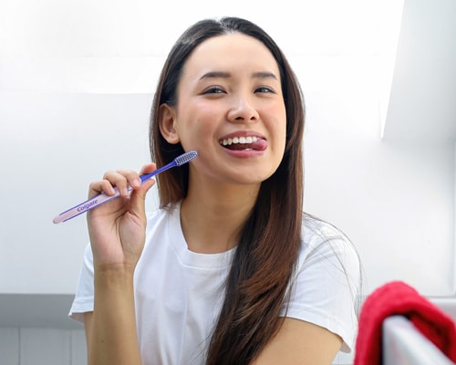 Wanita Asia tersenyum sambil memegang Berus Gigi Colgate SlimSoft Ortho
